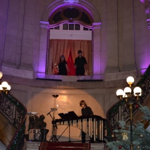 Zdjęcie przedstawia występujących artystów w witrynie okiennej oraz u szczytu schodów  wewnątrz Pałacu Kawalera,  podczas koncertu pt. Percussio
